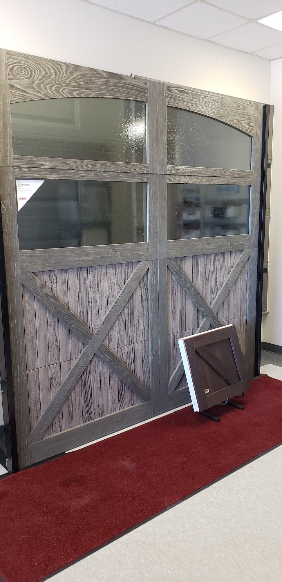 A decorative, wooden garage door with glass panels, a red rug, and a sample door.