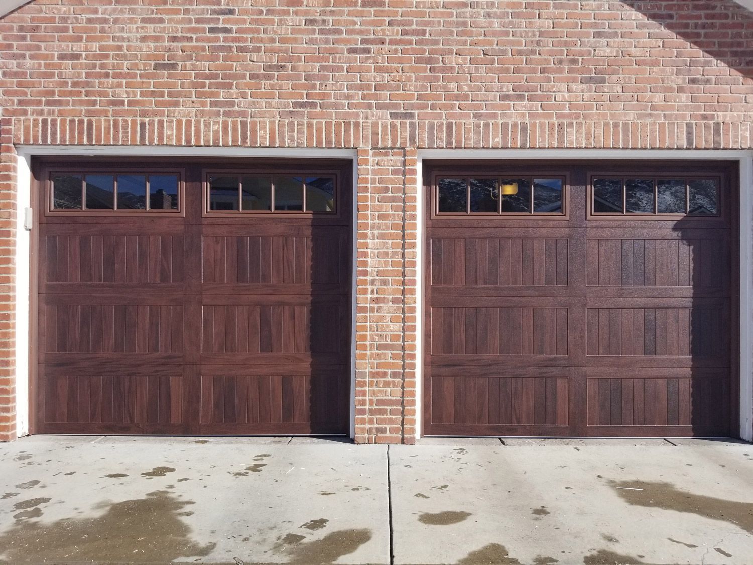 Two brown garage doors with windows in a brick building.