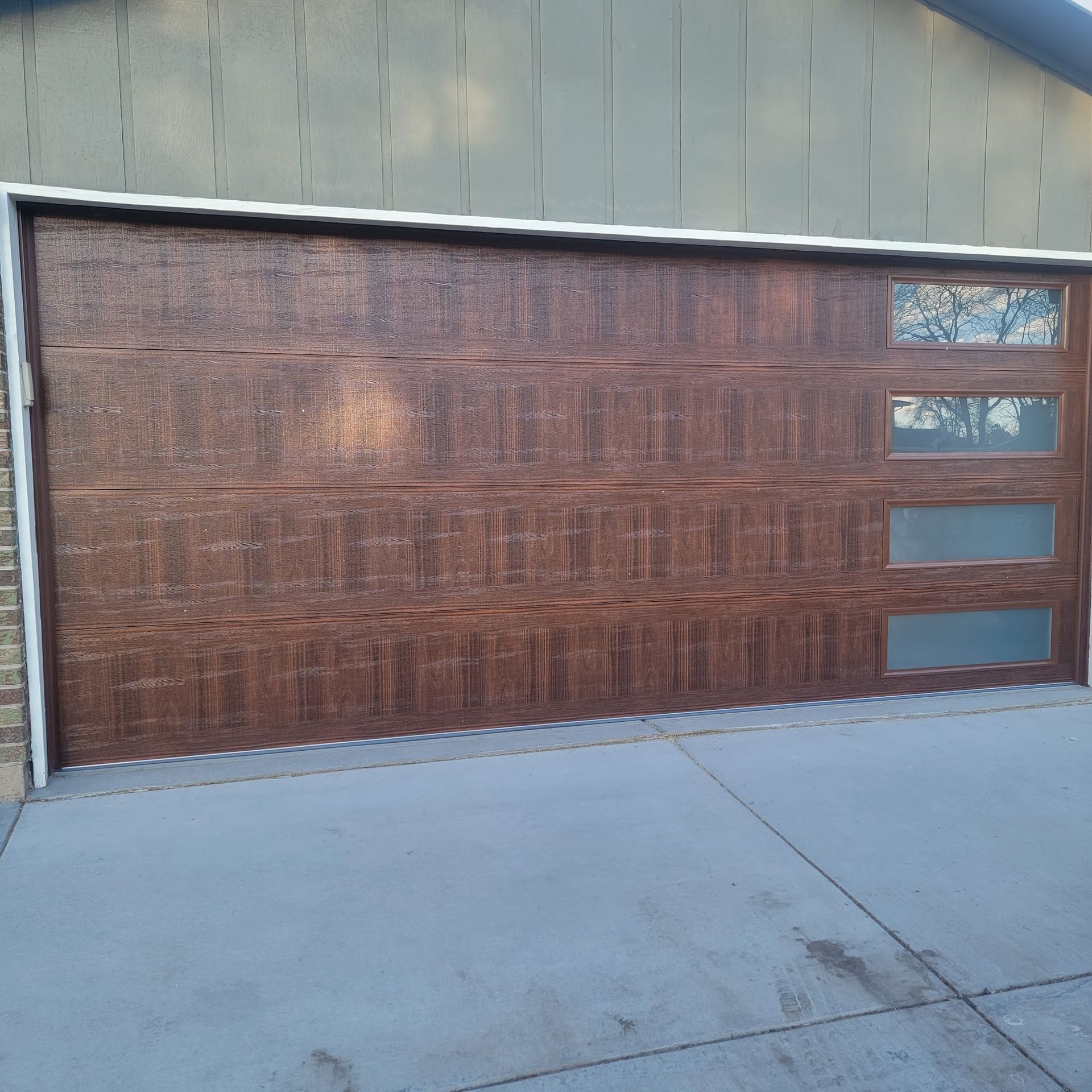 Brown garage door with three glass windows, on a concrete driveway.