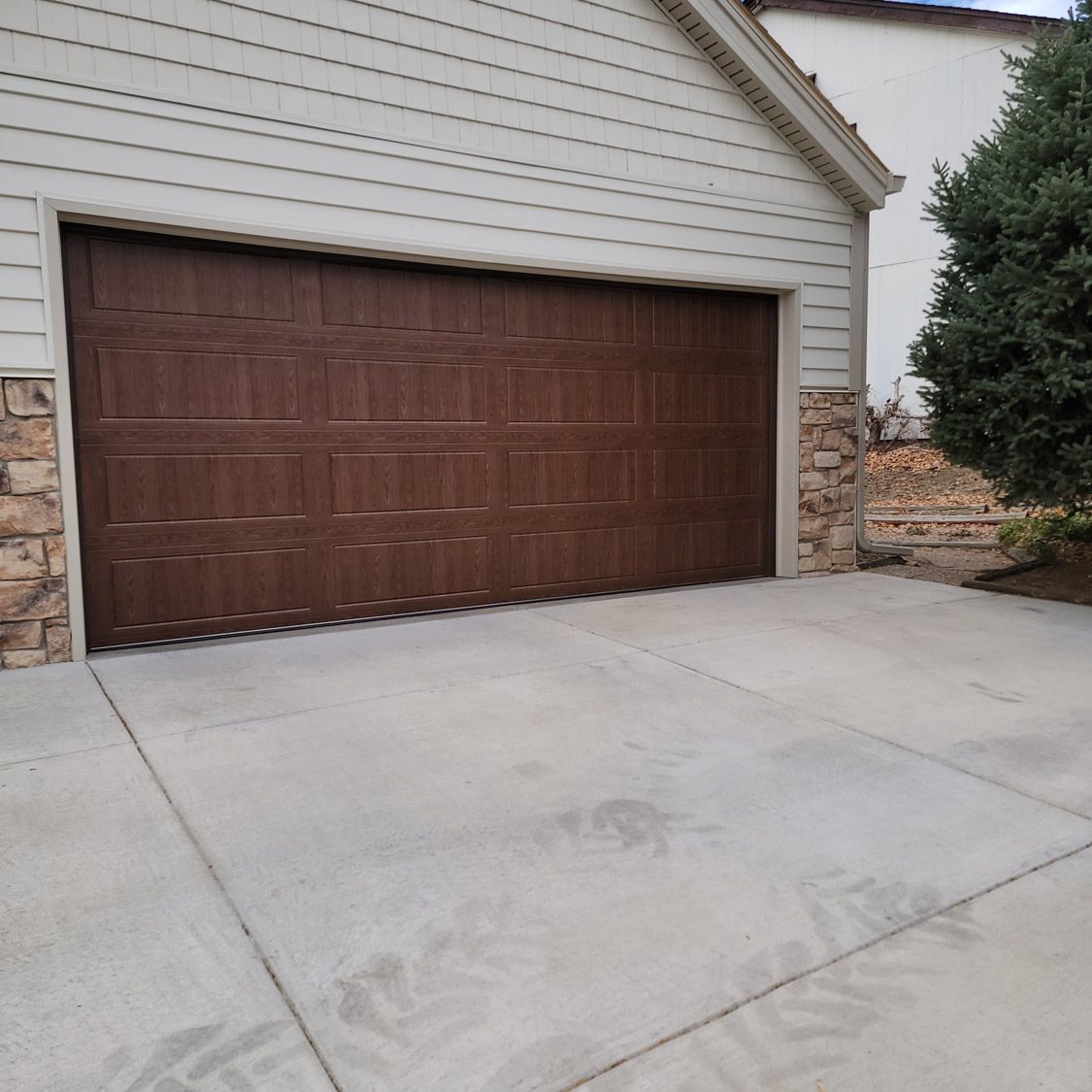 Brown garage door on a concrete driveway, with stone accents on the sides.