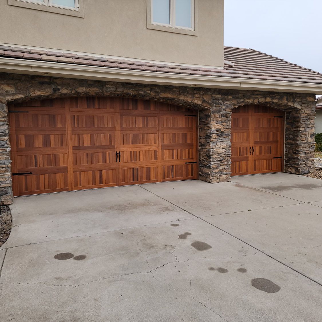 Two wooden garage doors under a stone archway, on a concrete driveway.