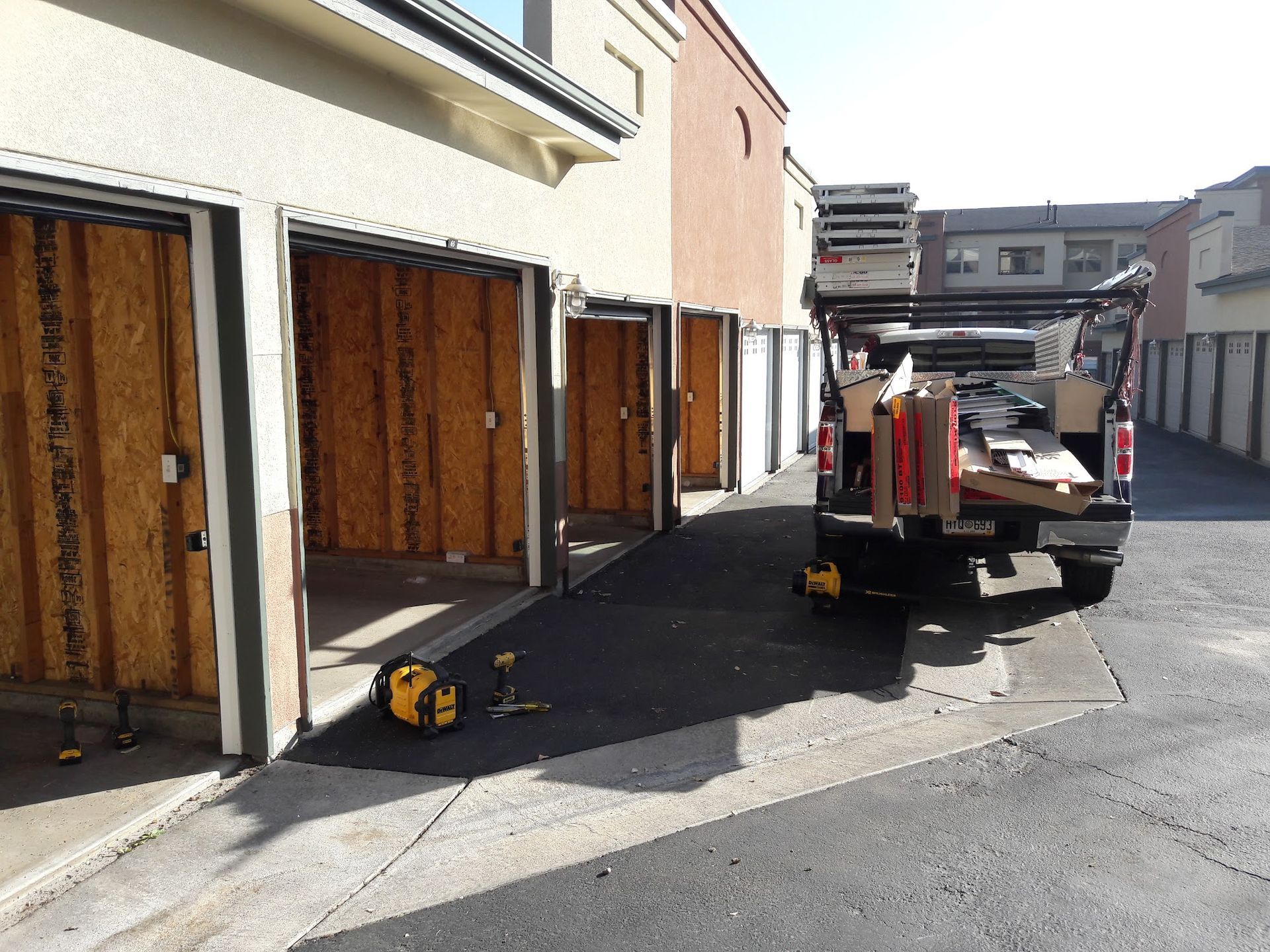 Truck parked near garages with open wooden doors; tools on ground.