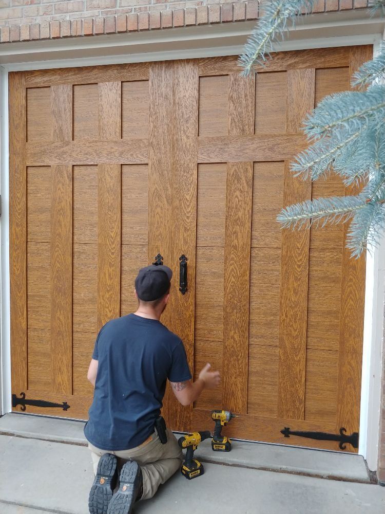 Man kneeling, working on a brown wooden garage door with black hardware.