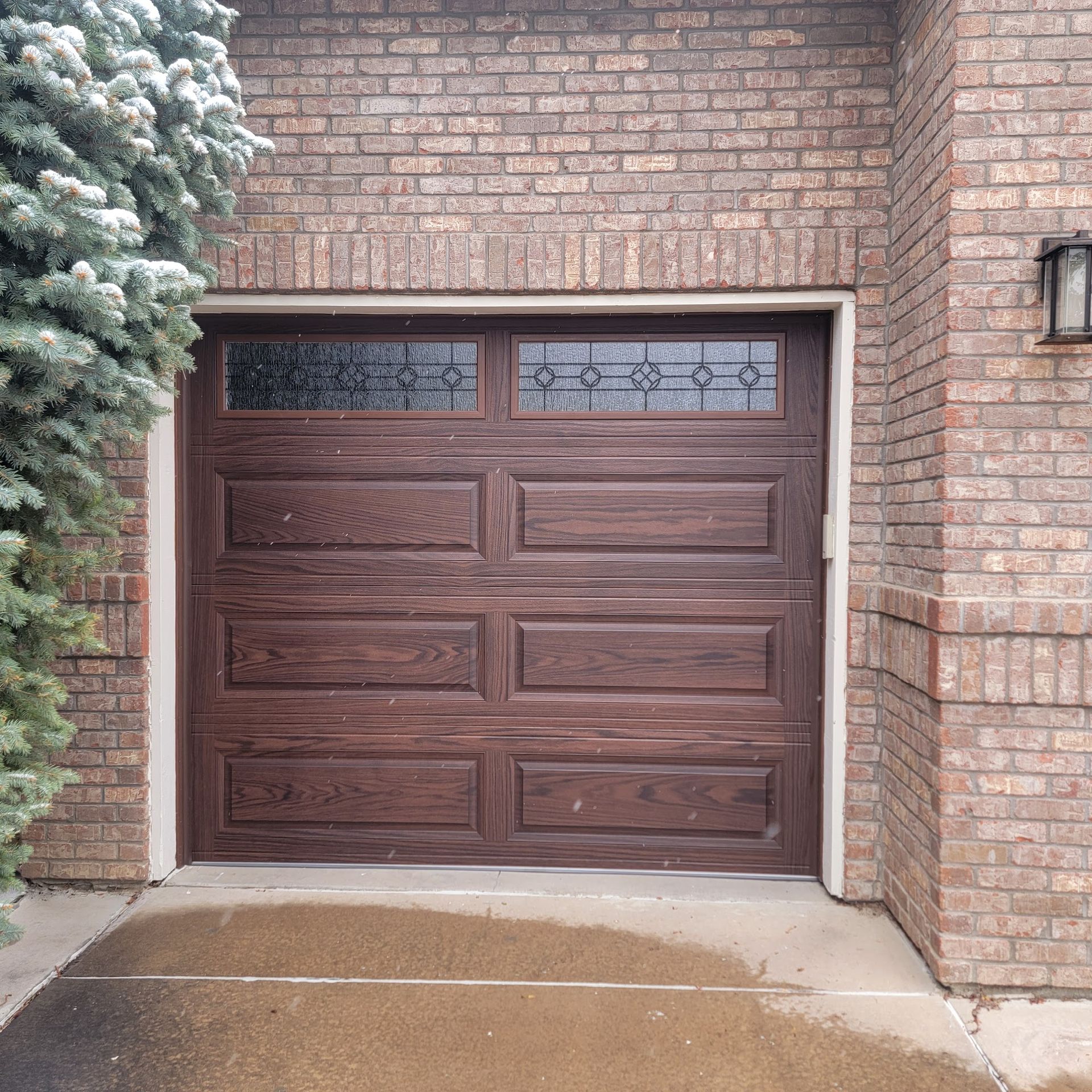Brown garage door with glass panels, surrounded by brick.