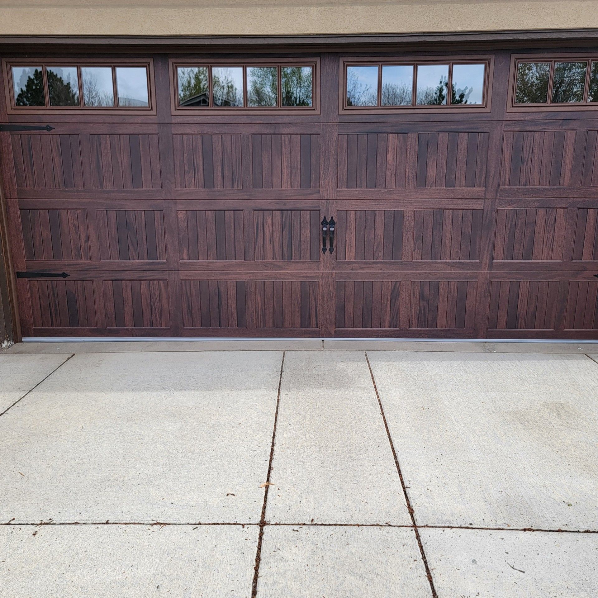 Brown wood-look garage door with windows above, set in a concrete driveway.
