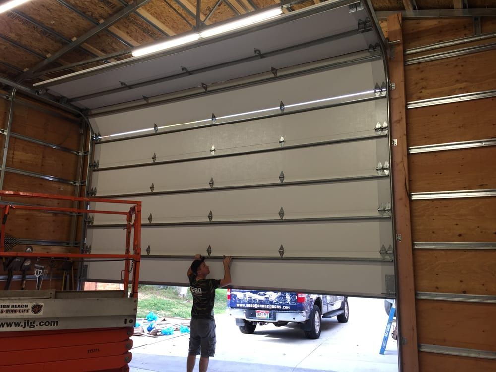Person adjusting a white garage door in an open bay. A truck is parked outside.
