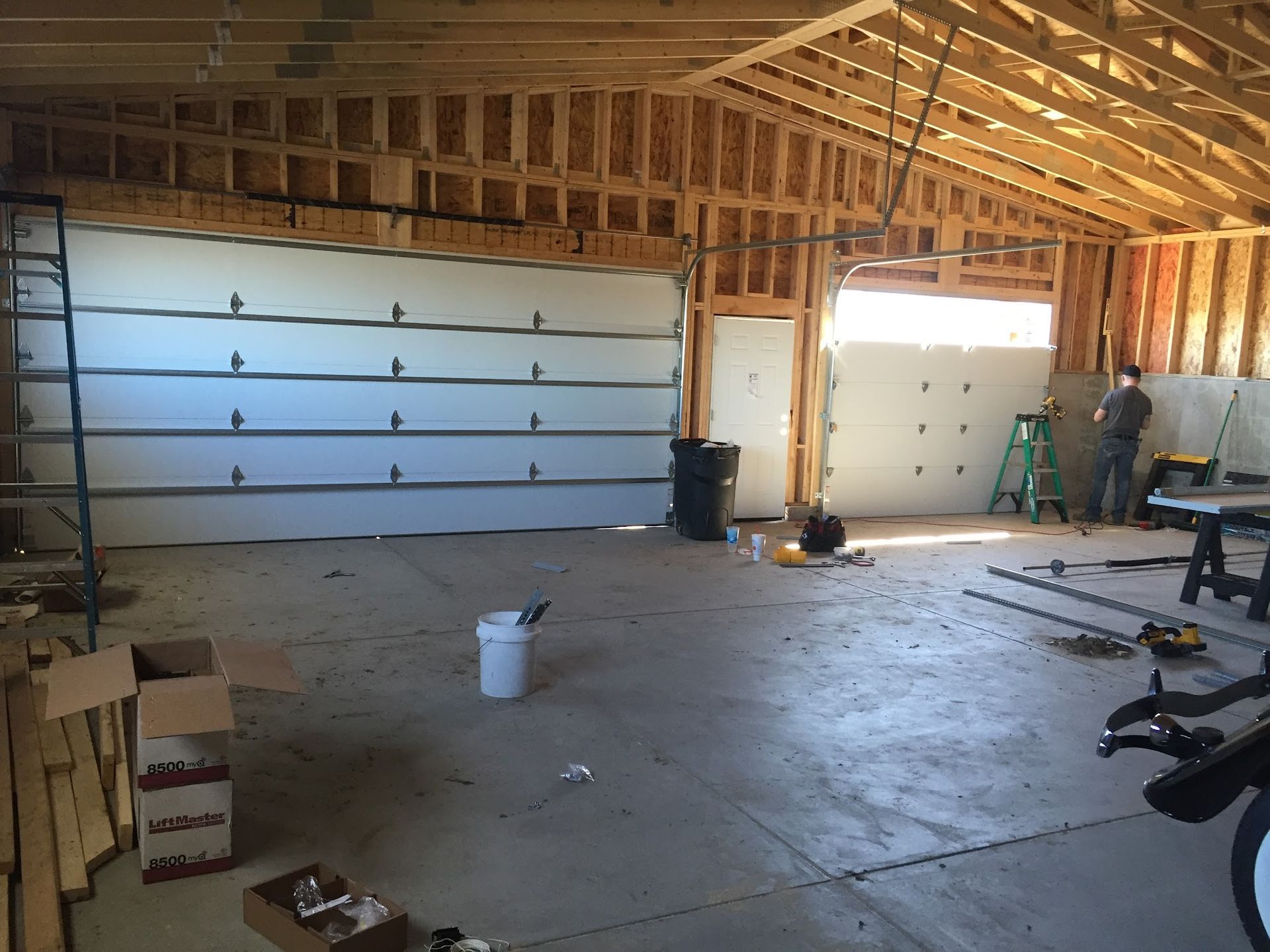 Interior of a garage under construction, with two garage doors and a worker.