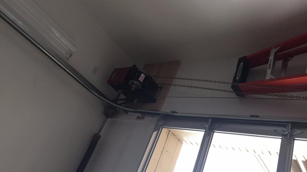 Garage door opener mounted on a wall, chain visible. Fluorescent light and door frame also shown.