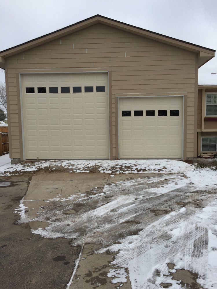 Tan building with two garage doors, sidewalk, and patches of snow.