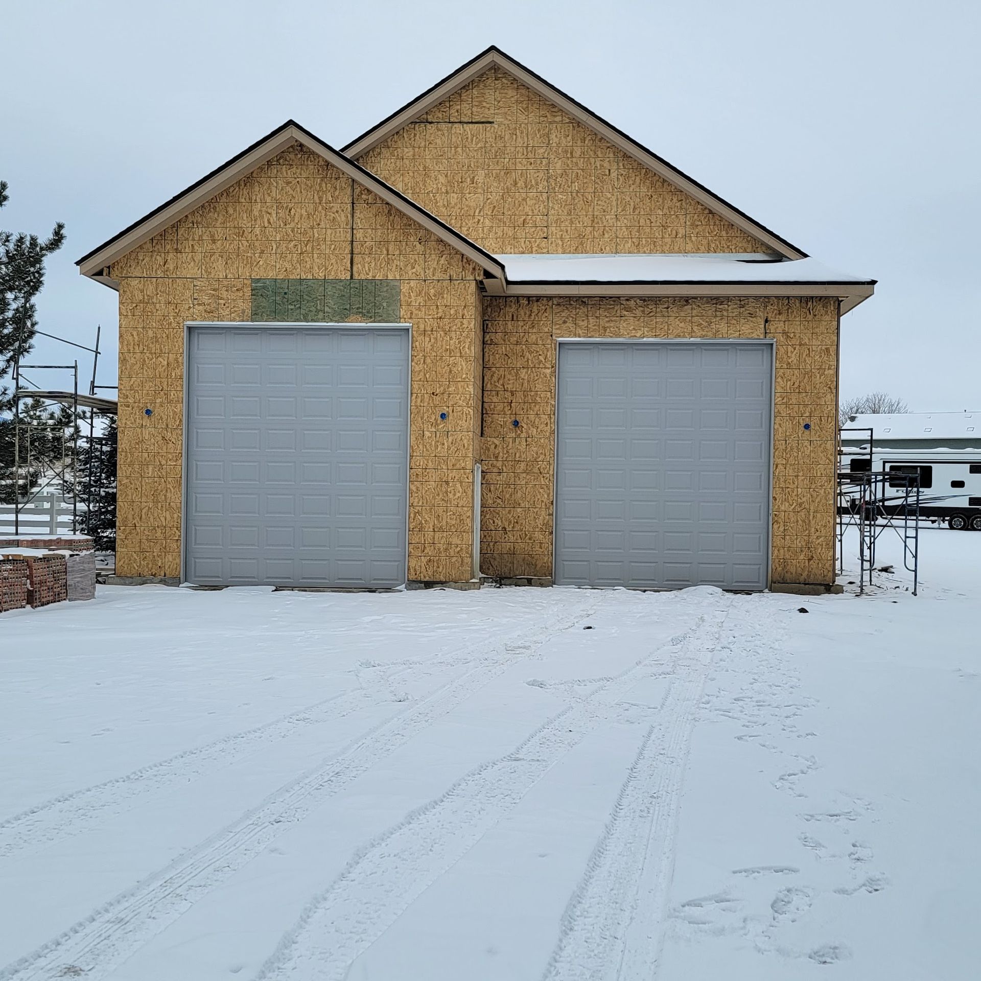 Garage under construction with two gray doors in a snowy setting.