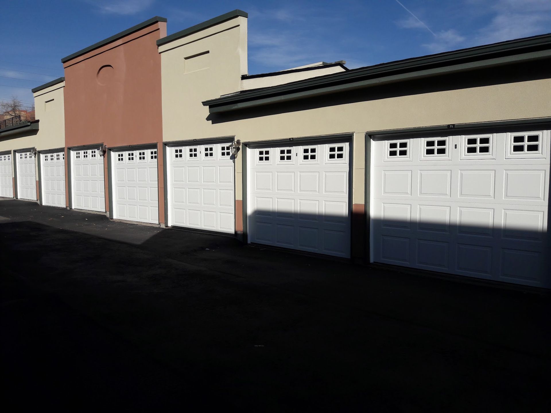 Row of white garage doors in a tan building under a blue sky.