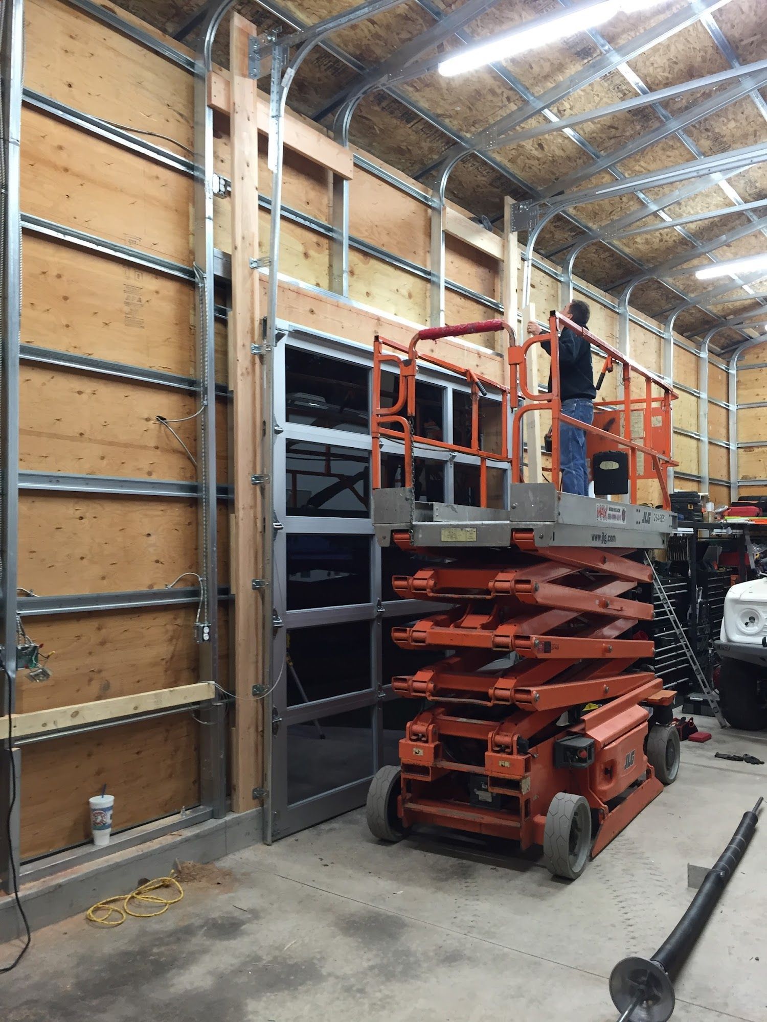 Man on lift working on garage door frame, wood and metal construction.