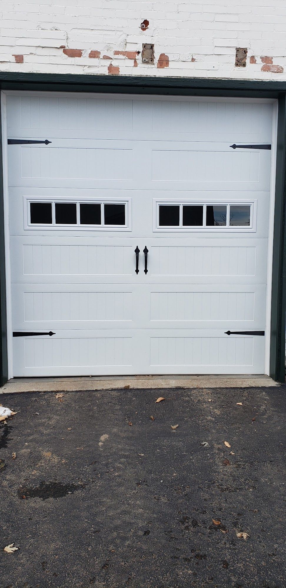 White garage door with black hardware and windows. Asphalt driveway in front.