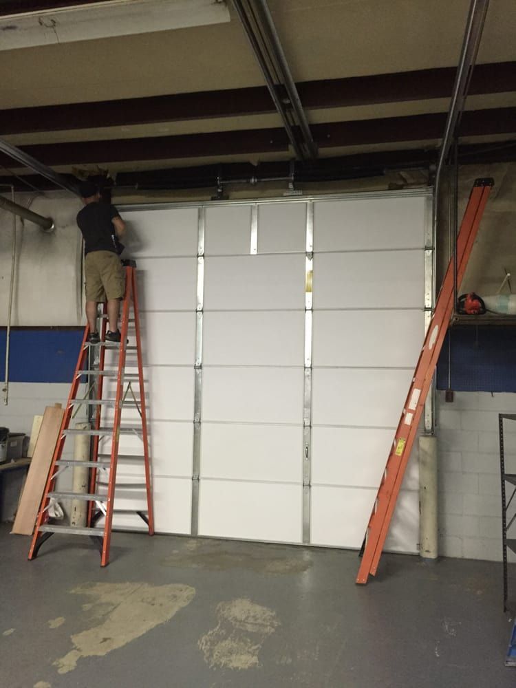 Person on ladder installing garage door, another ladder leaning against door in a garage.