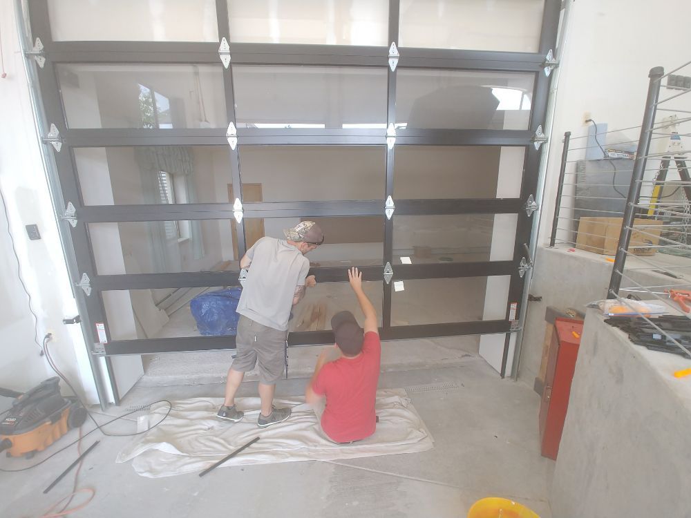 Two people installing a glass garage door in a partially constructed building.