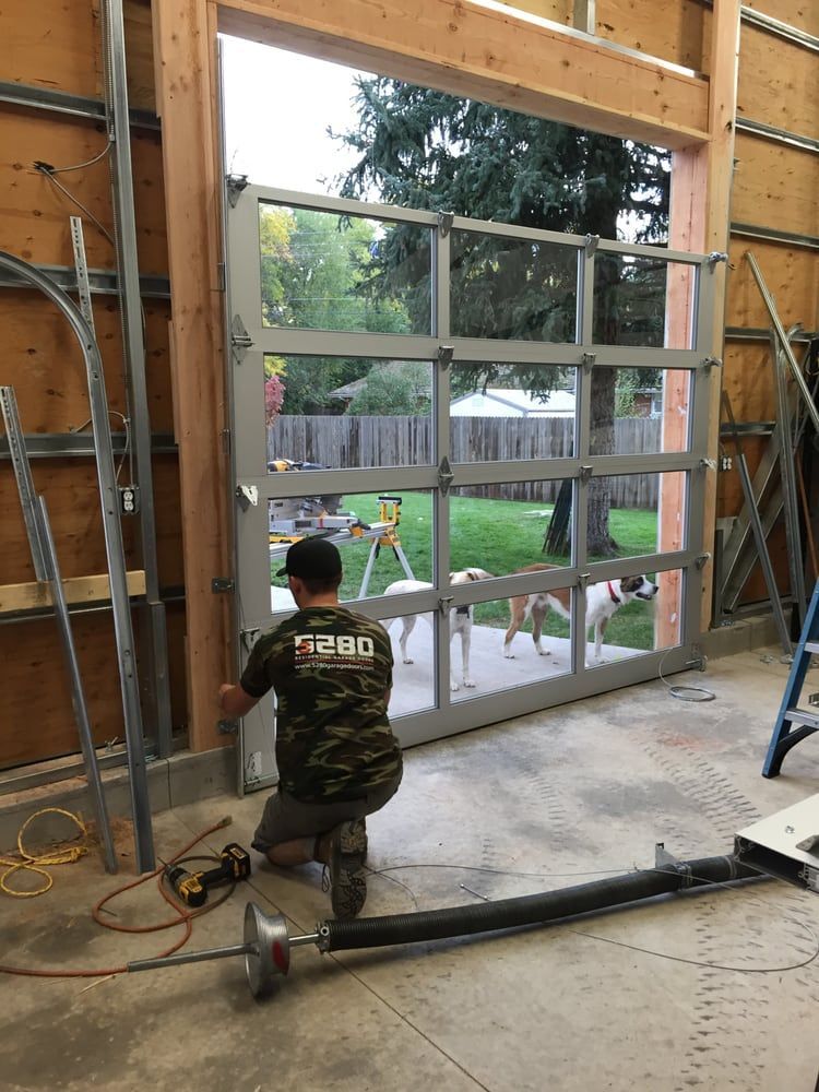 Man installs a glass garage door. The backyard with trees is visible through the door.