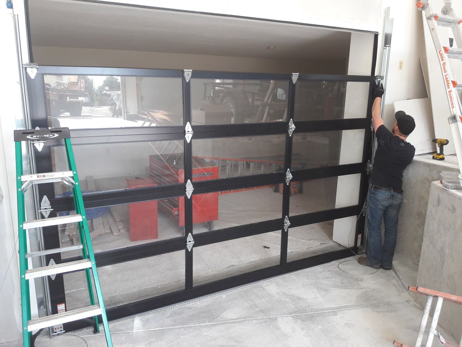 Person installing a black screen garage door; interior setting with tools and ladder.