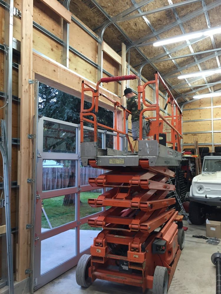 Person on a lift installing a glass garage door in a garage under construction.