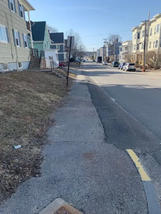 A sidewalk along the side of a street with a yellow curb.