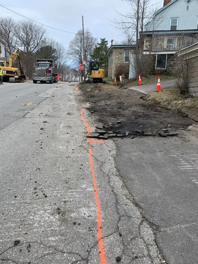 A yellow truck is driving down a street next to a house.