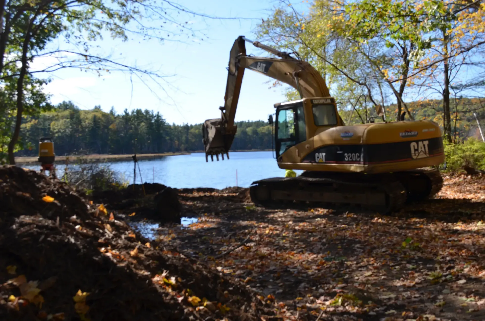 A cat excavator is digging in the dirt near a lake.