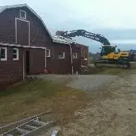A bulldozer is moving dirt in front of a barn.