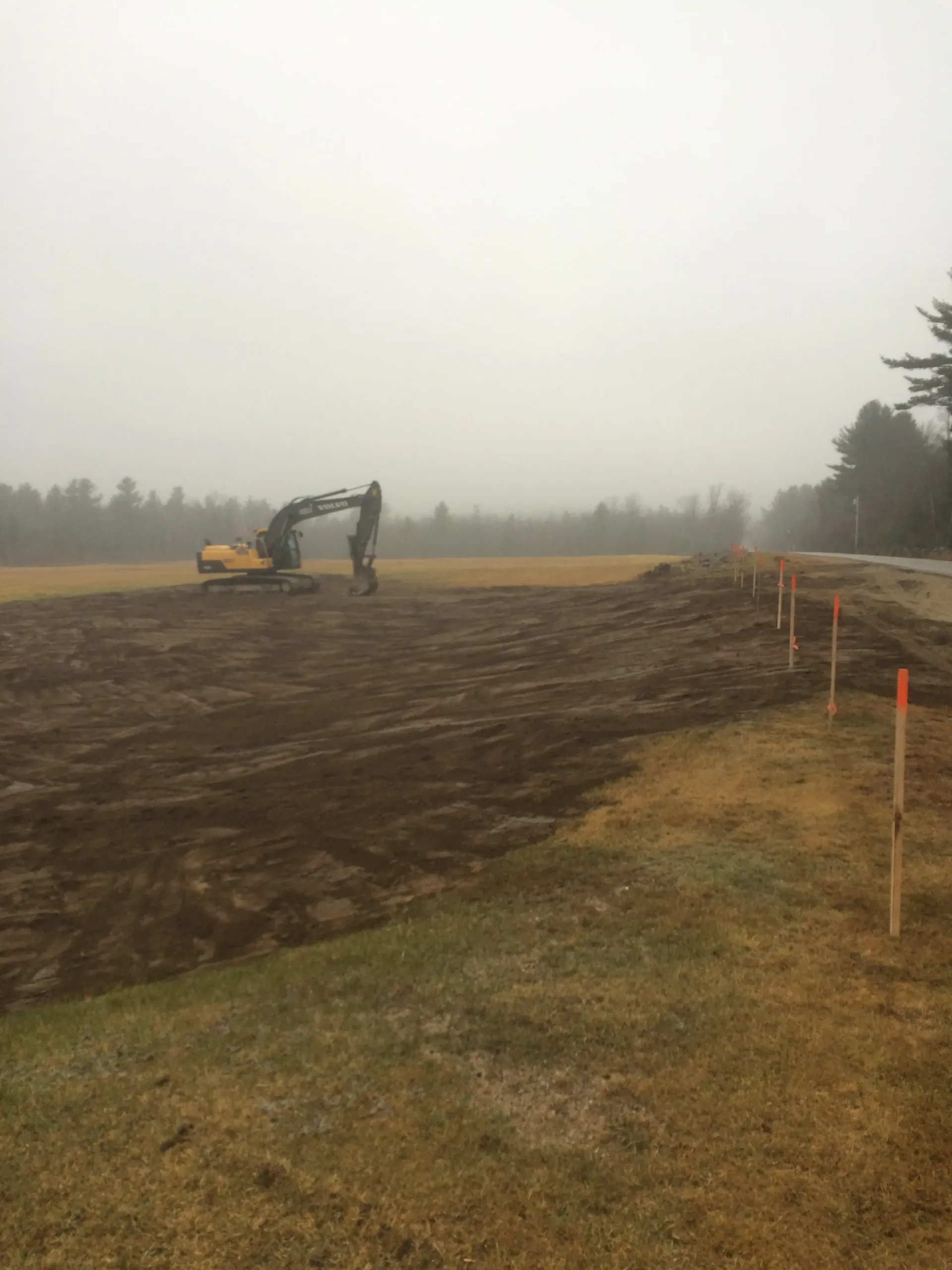 An excavator is moving dirt in a field on a foggy day.