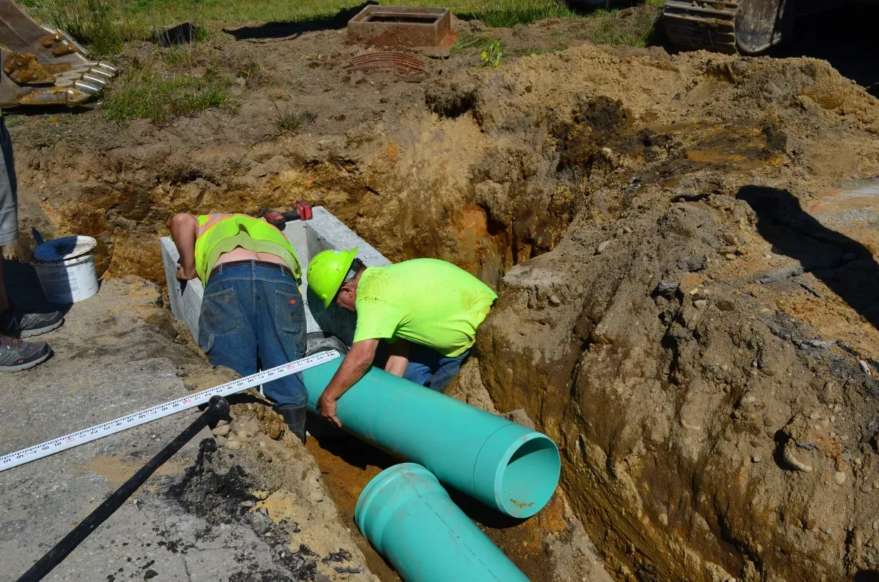 Two men are working on a green pipe in the dirt.