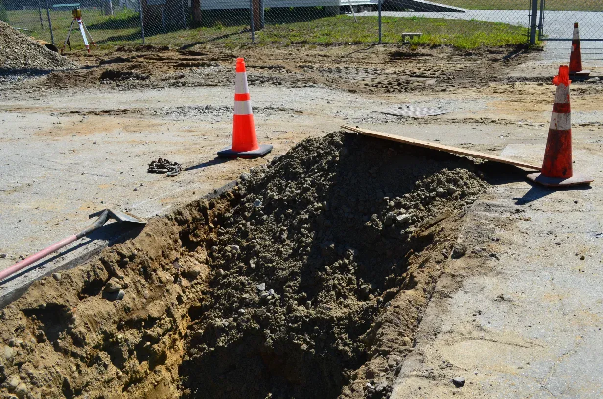 A construction site with a hole in the ground and orange and white traffic cones