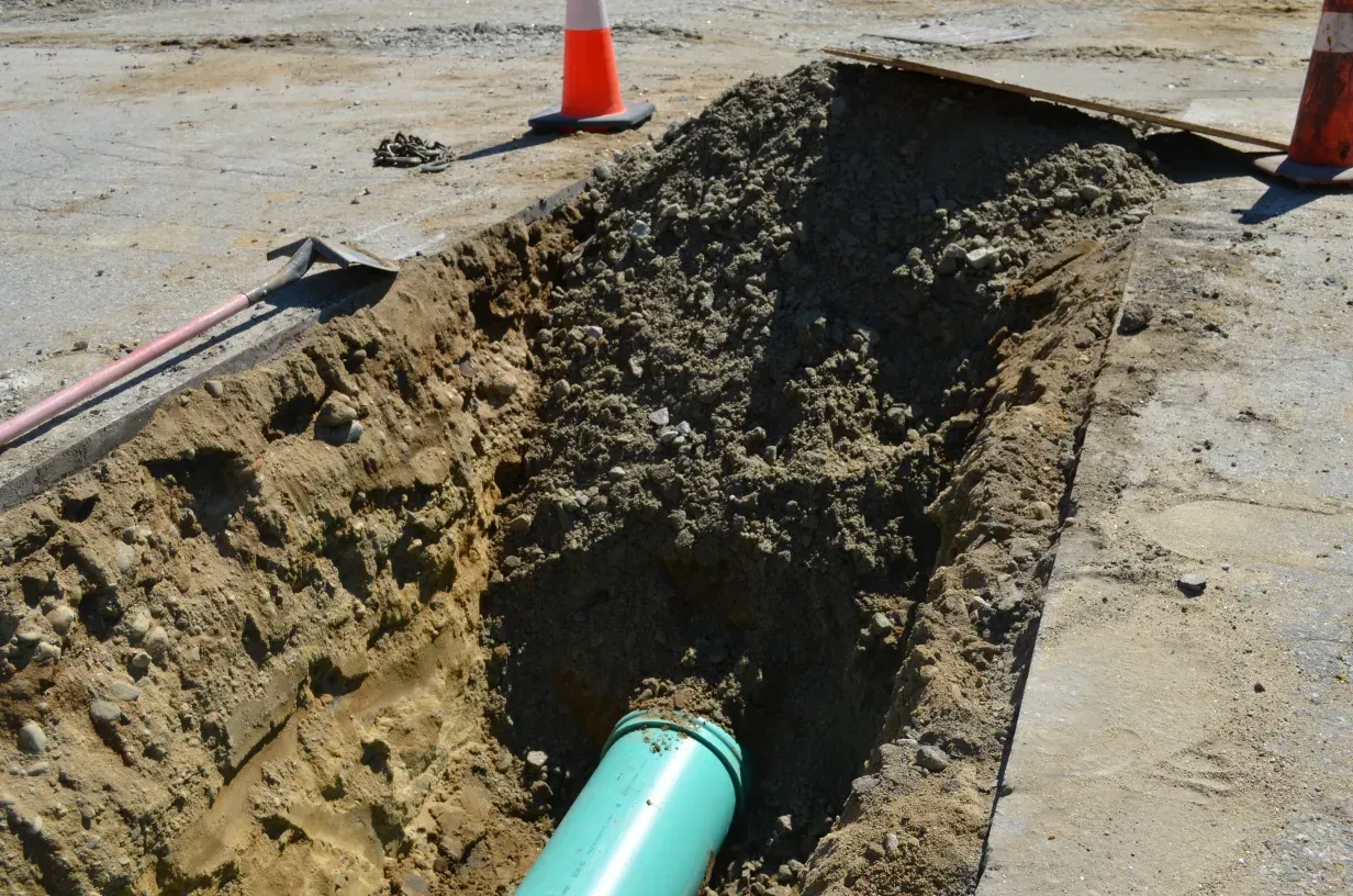 A green pipe is being installed in the dirt