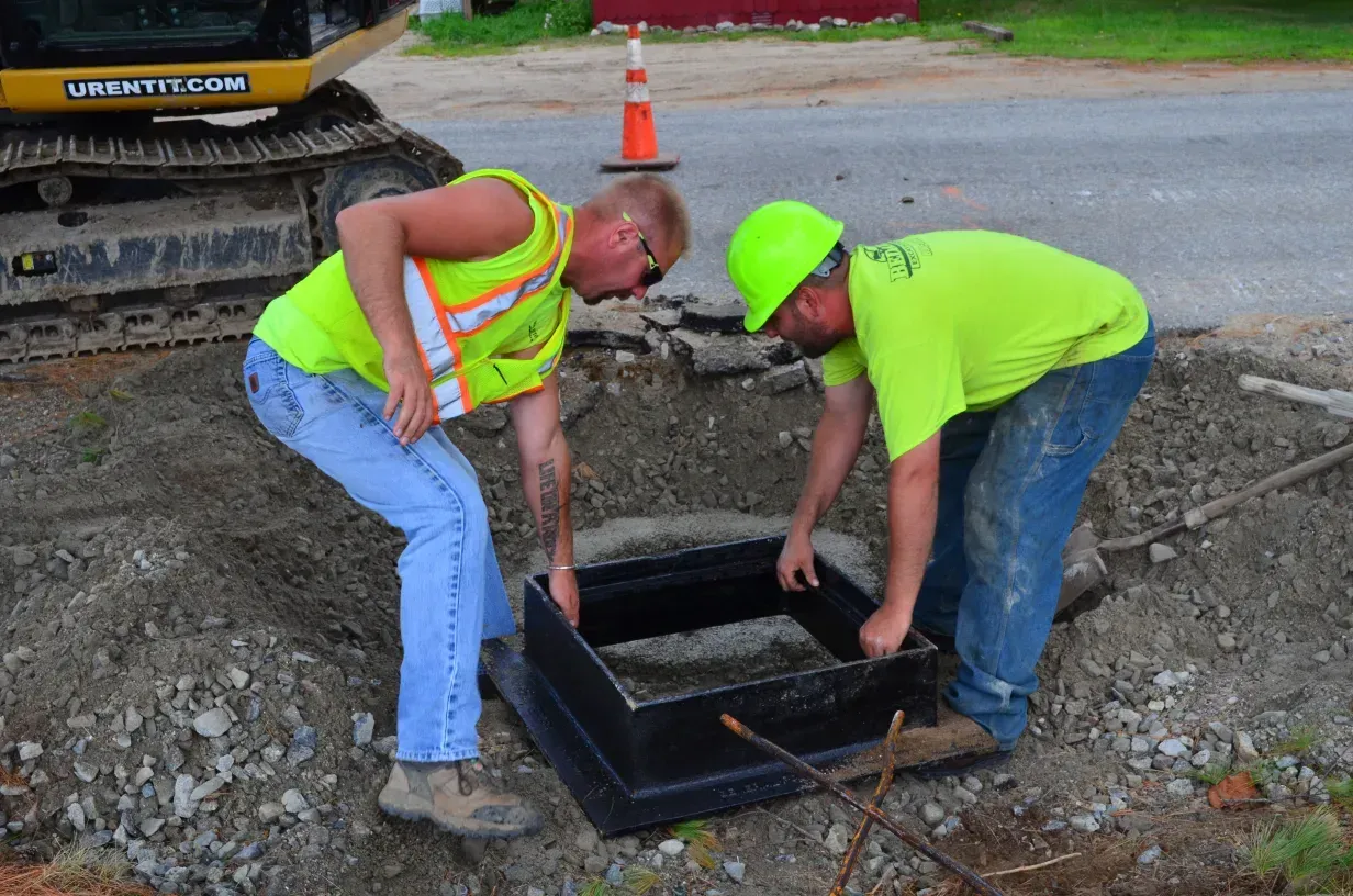 Two construction workers are working on a manhole cover