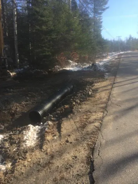 A large black pipe is laying on the side of a road.