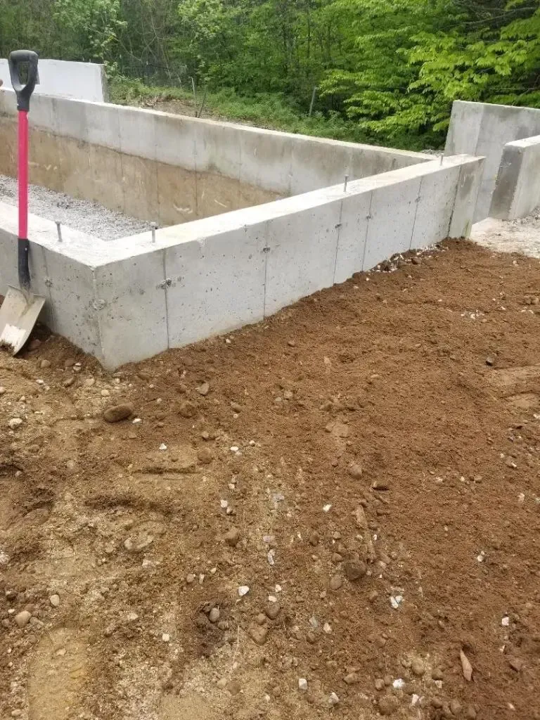 A shovel is sitting on top of a pile of dirt next to a concrete wall.