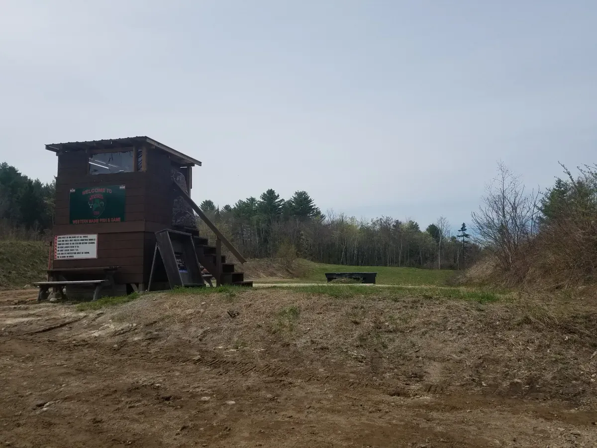 A small wooden building with stairs is in the middle of a field.