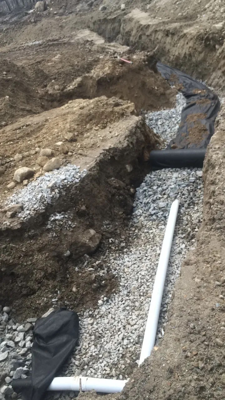 A pipe is laying in the dirt next to a pile of gravel.