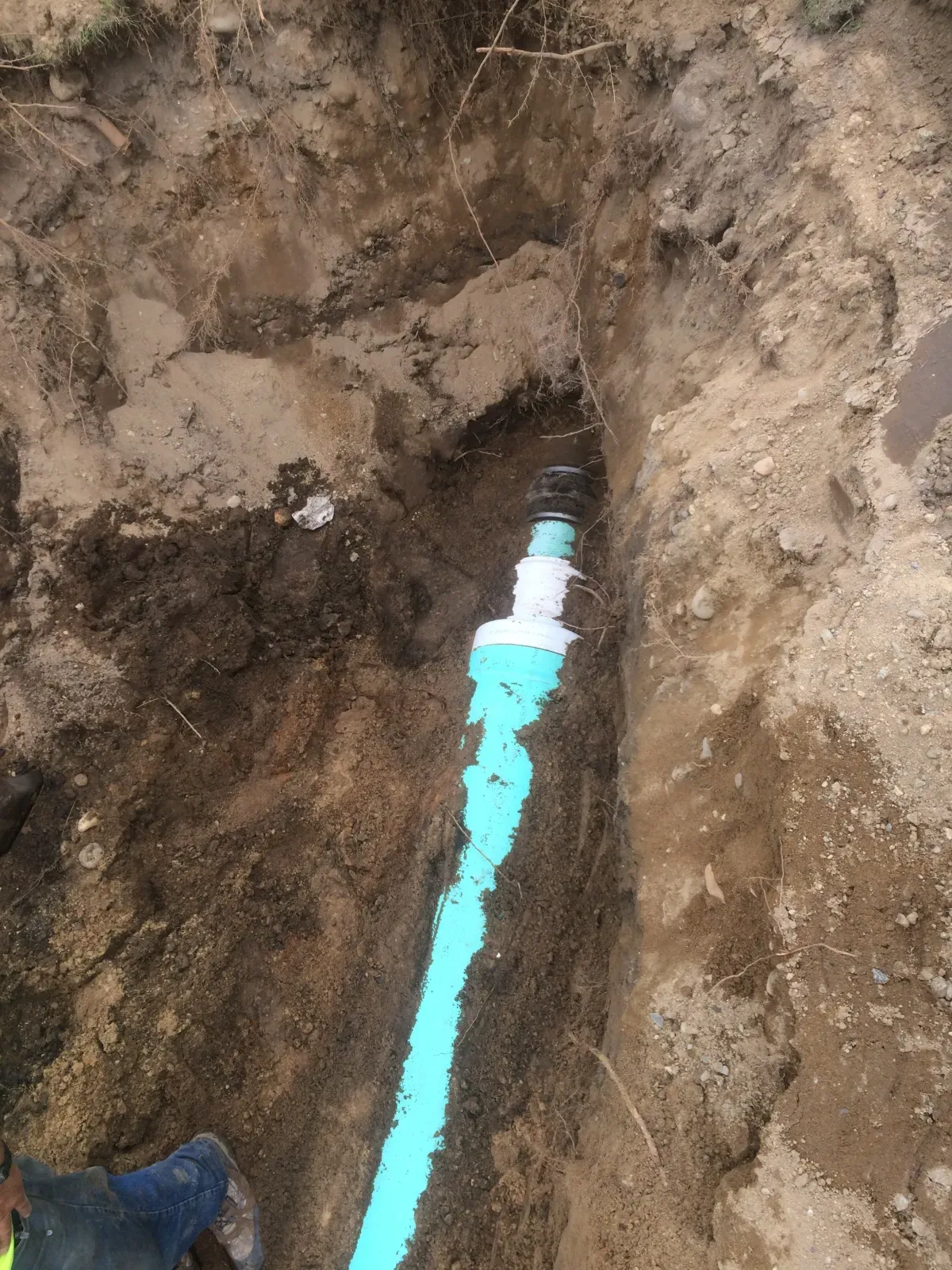 A blue pipe is being installed in the dirt.