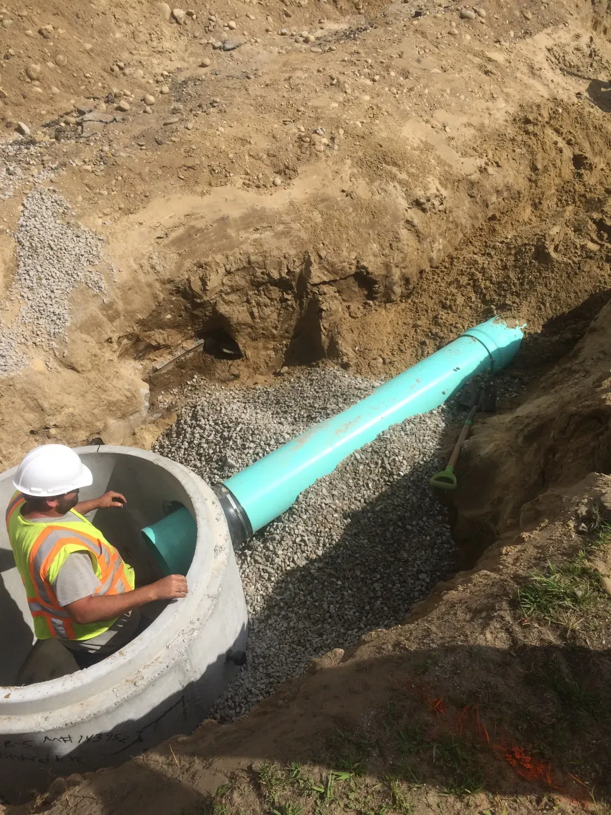 A man is sitting in a manhole next to a green pipe.