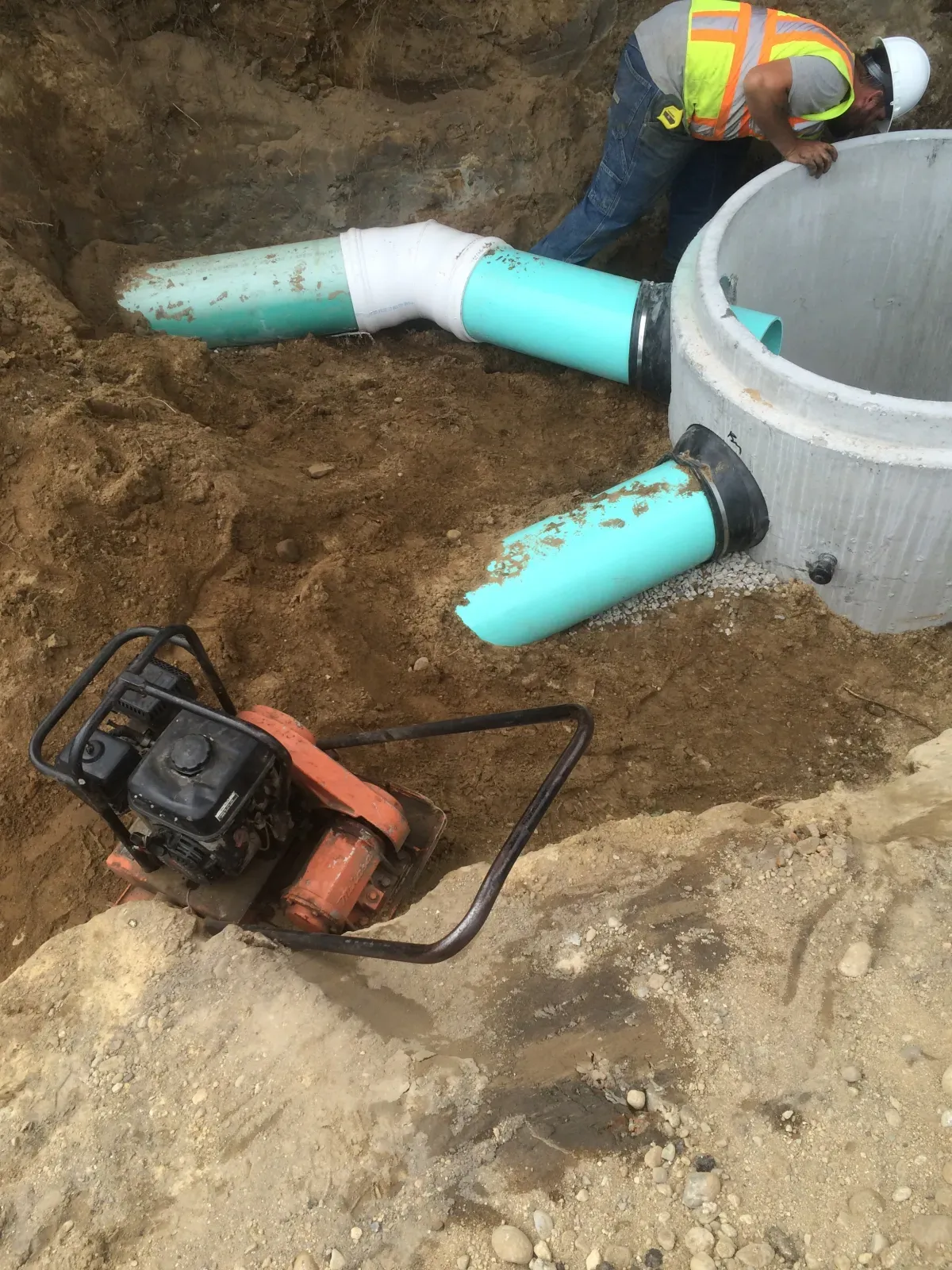 A man is working on a drainage system in the dirt.