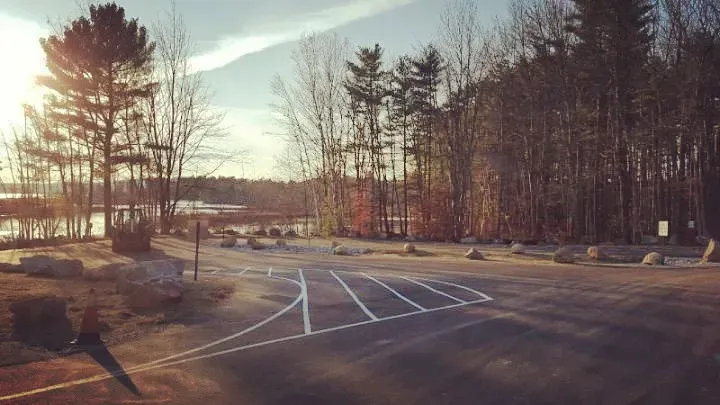 A parking lot with trees in the background and the sun shining through the trees.