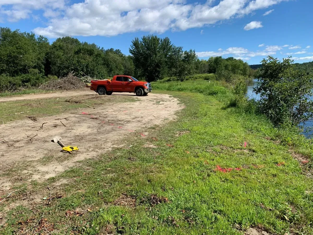 A red truck is parked on a dirt road next to a body of water.