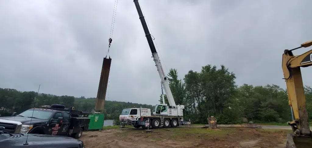 A crane is lifting a piece of wood in a field.