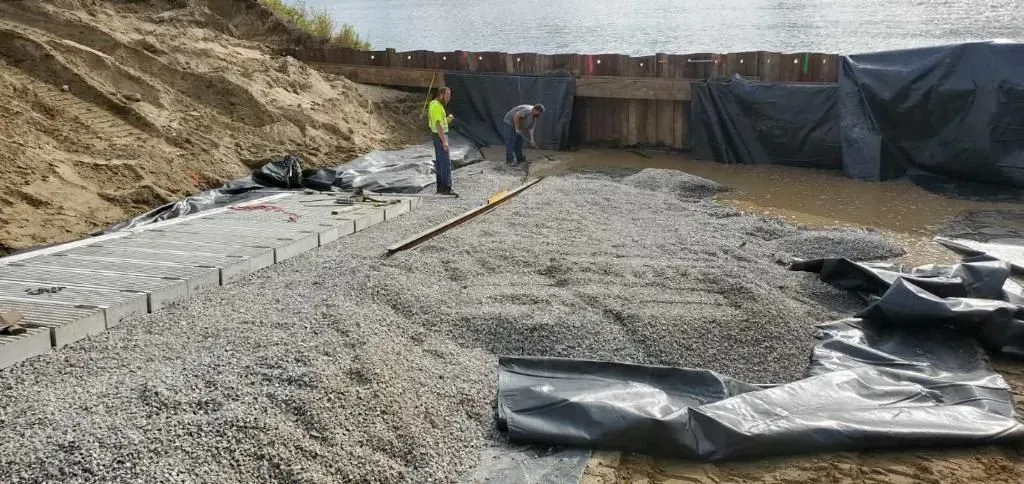 A man is standing on a pile of gravel next to a body of water.