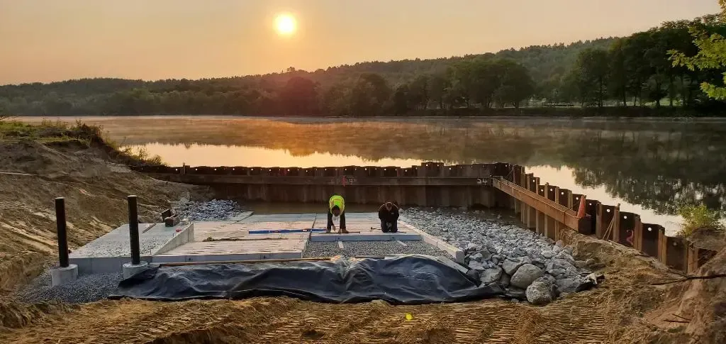 A construction site next to a lake with a sunset in the background.