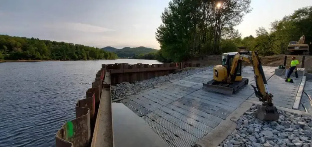 A large yellow excavator is working on a bridge over a body of water.