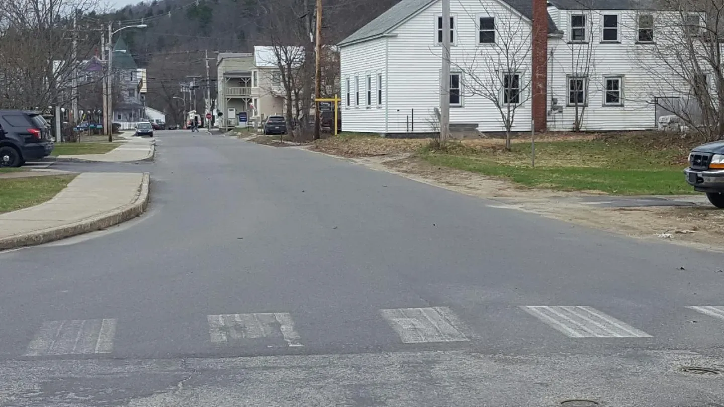 A car is driving down a street with a white house in the background.