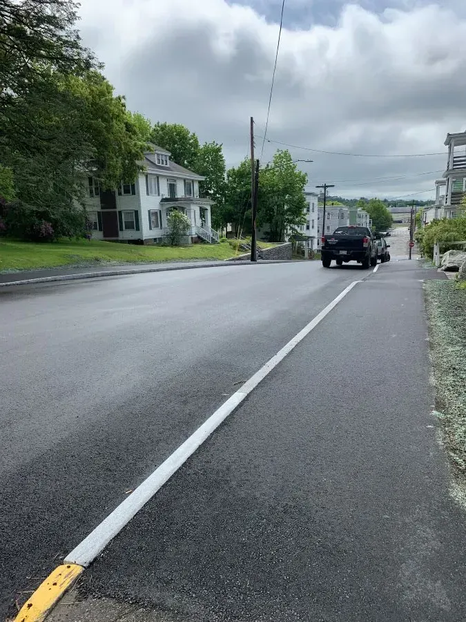 A black truck is driving down a street with houses in the background