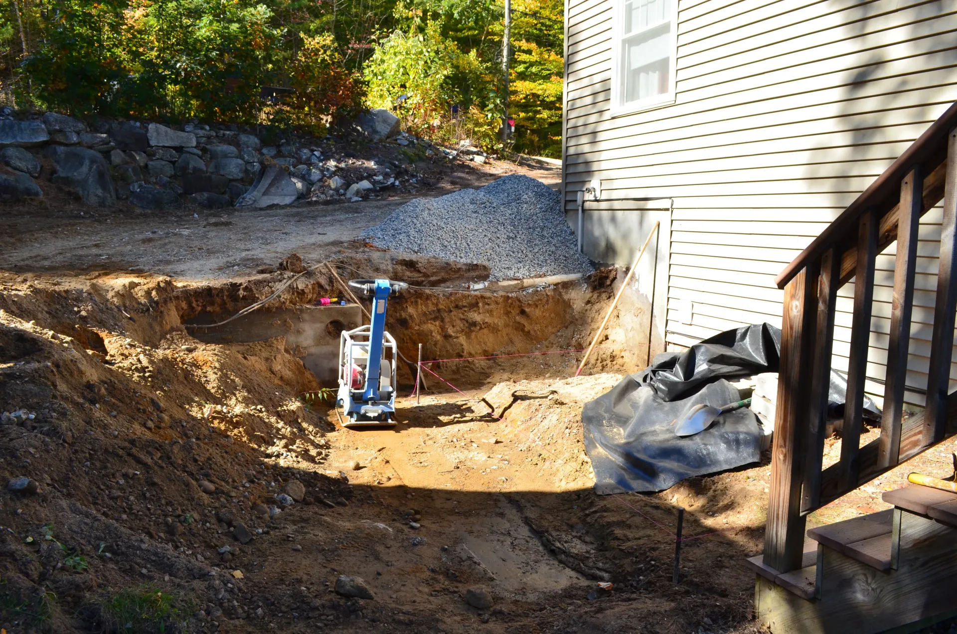 A machine is digging a hole in the dirt in front of a house.