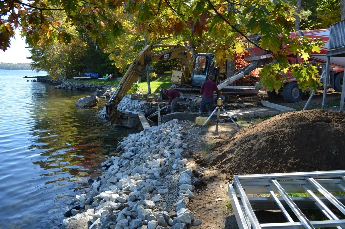 A man is working on a rocky shoreline next to a body of water.