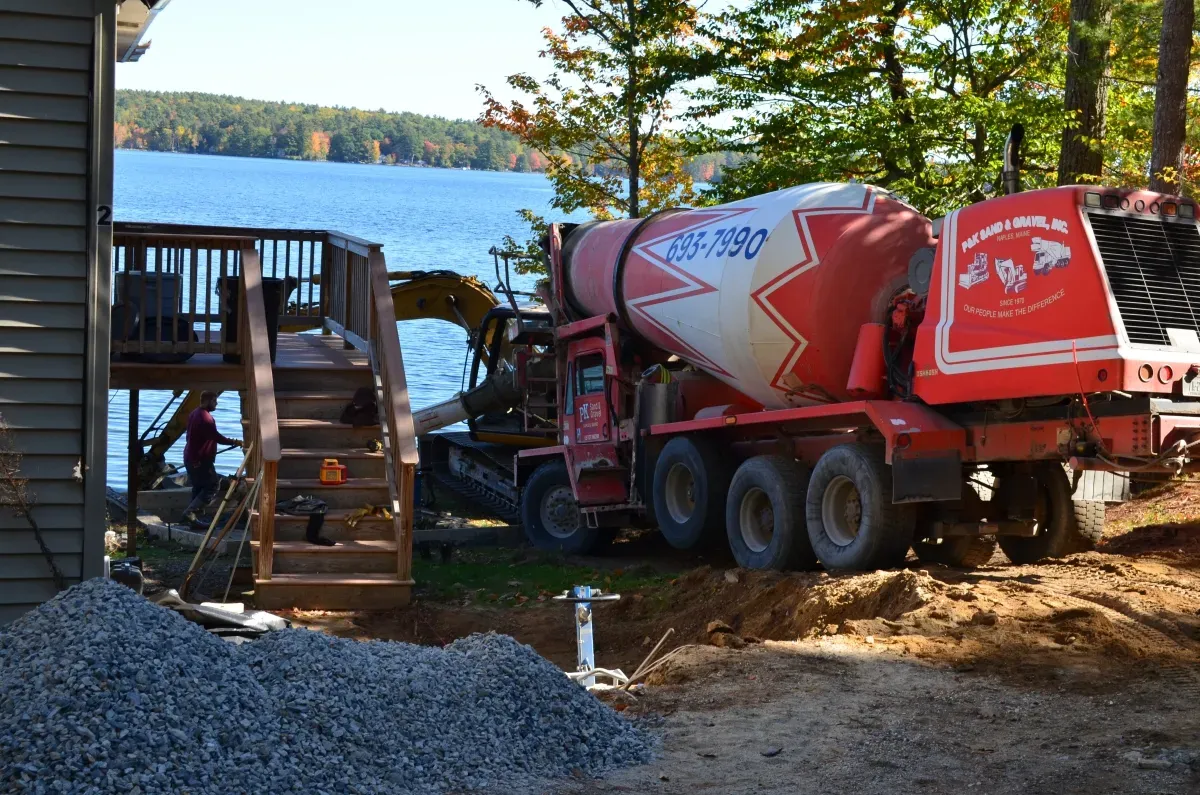A red and white concrete mixer truck is parked in front of a lake