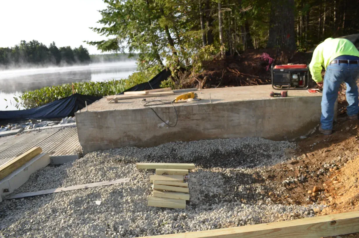 A man is working on a concrete structure near a lake